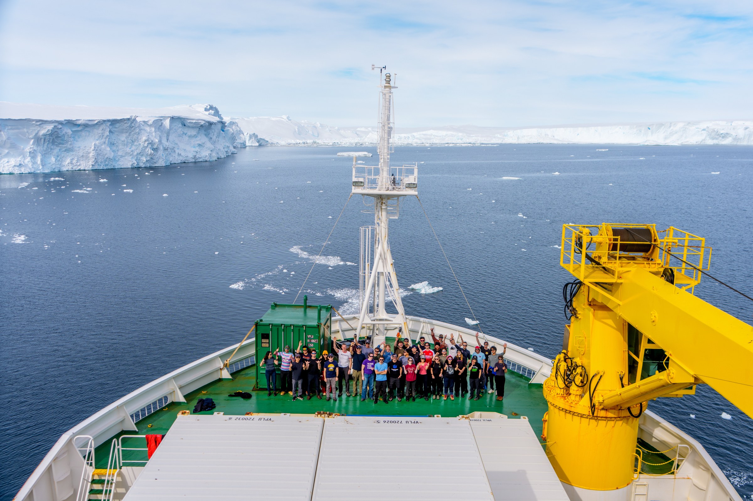 The international team of the 2025–26 Thwaites Glacier expedition gathered on the RV Araon foredeck, with the Antarctic ice shelf in the distance.